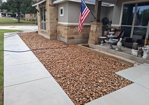 Finished rock bed along a front walkway in front of a stone home